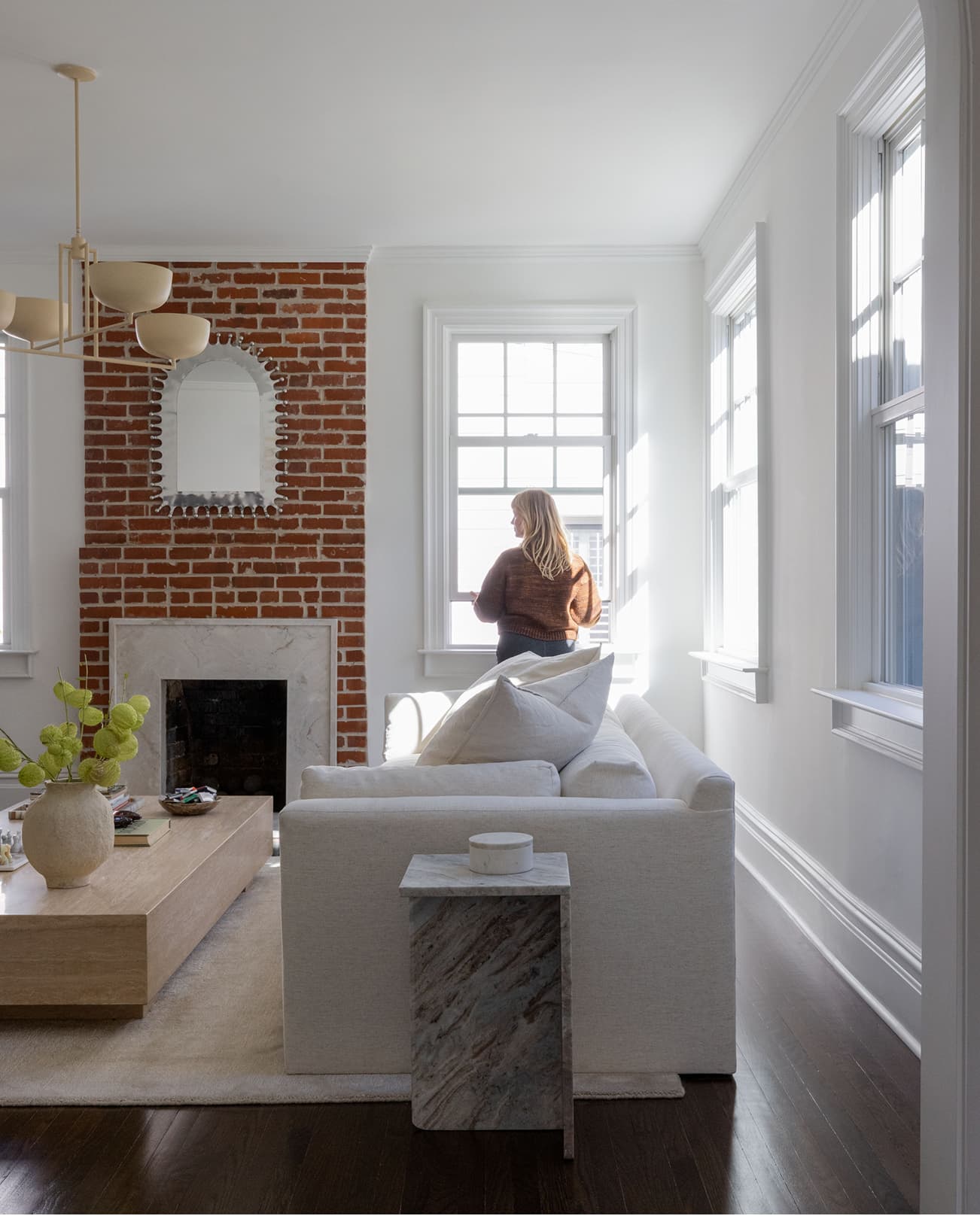 A woman opens a white Marvin Elevate Double Hung window in a living room next to a small brick fireplace.