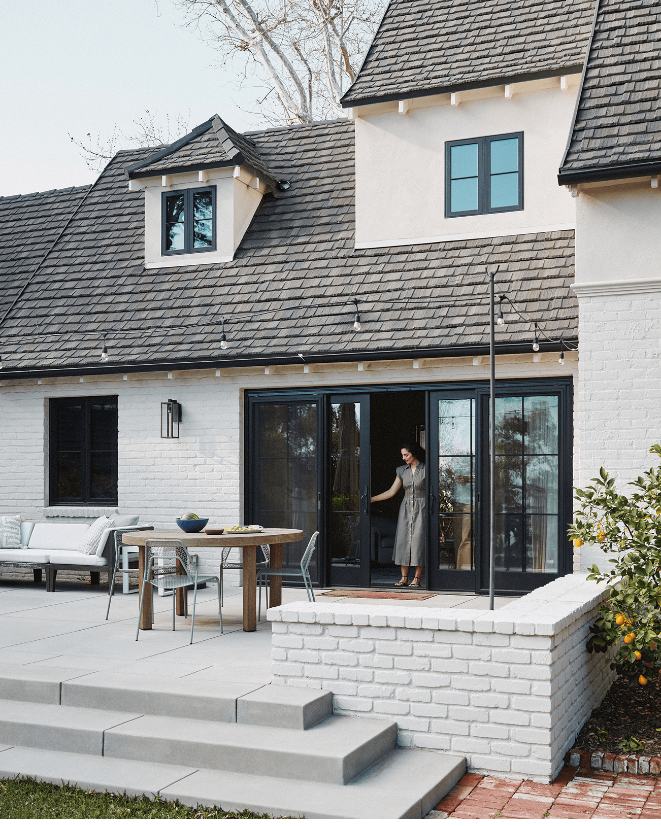 White brick home exterior with a woman opening a black Marvin Ultimate Sliding Door.