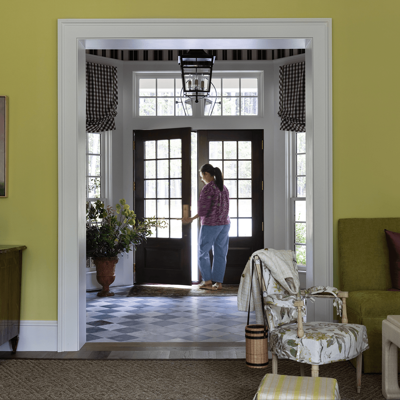 A woman opens a large Marvin Ultimate Wood Inswing French door with divided lites from an entry way.