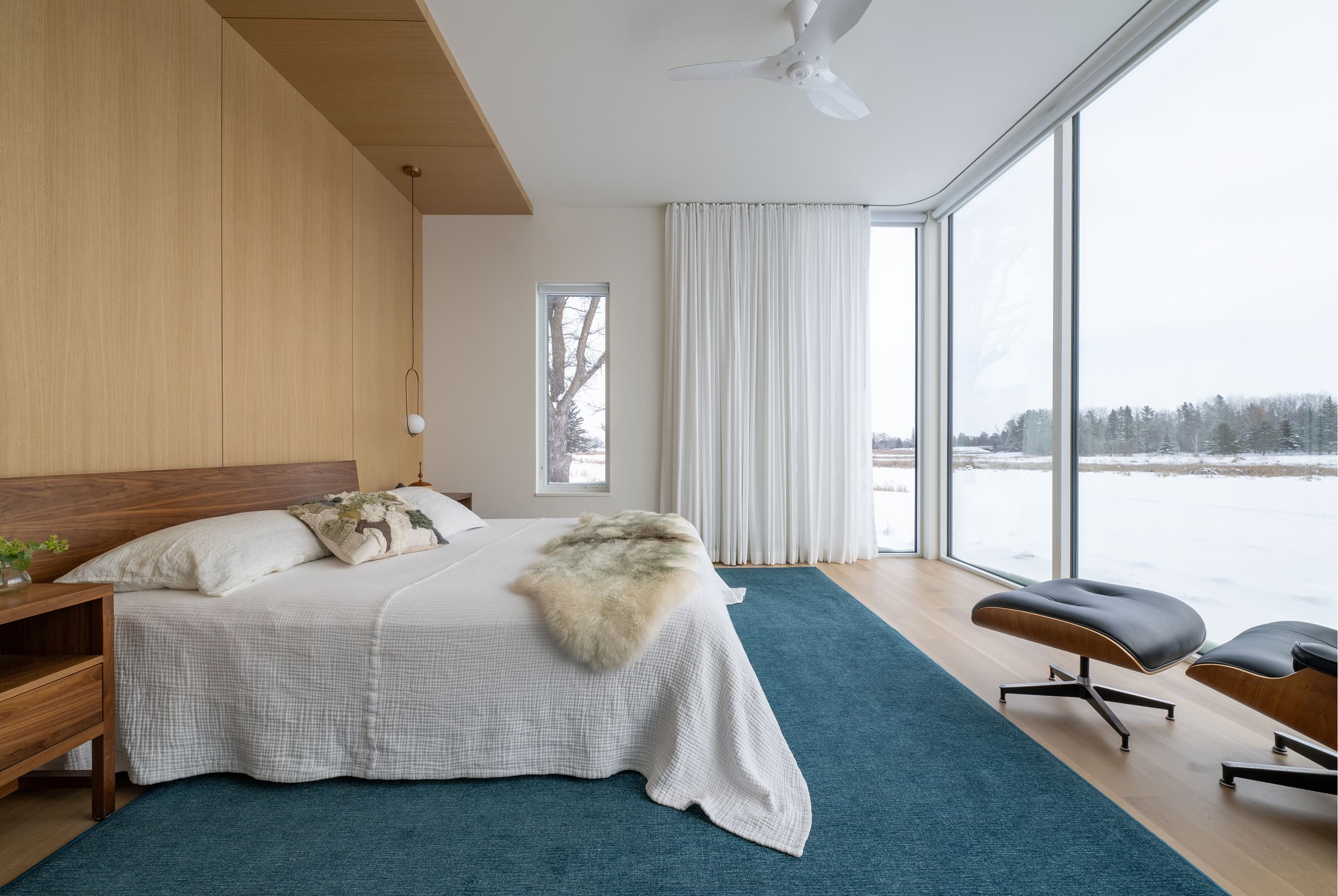 Bedroom interior with large white Marvin Modern Direct Glaze windows looking out to a frozen lake and timbers.